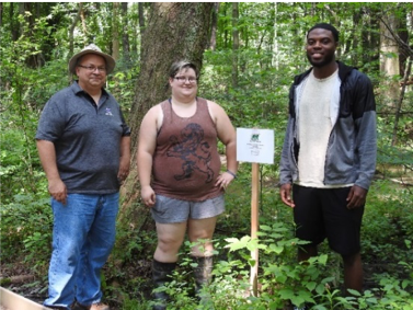Two students and a faculty member stand next to sign near a Nature Center trail